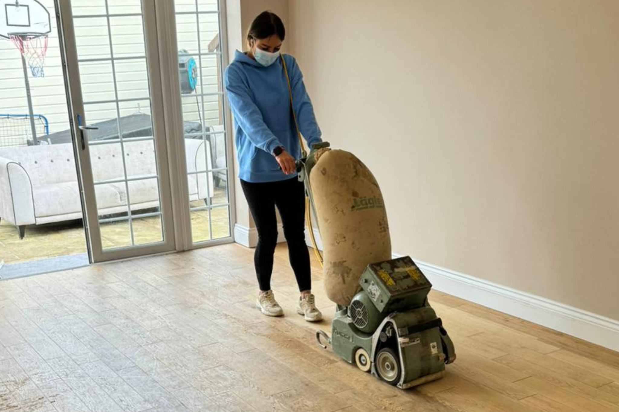 Technician sanding engineered oak plank Hardwood Floors in an Eltham living room with a drum sander and dust-extraction bag.