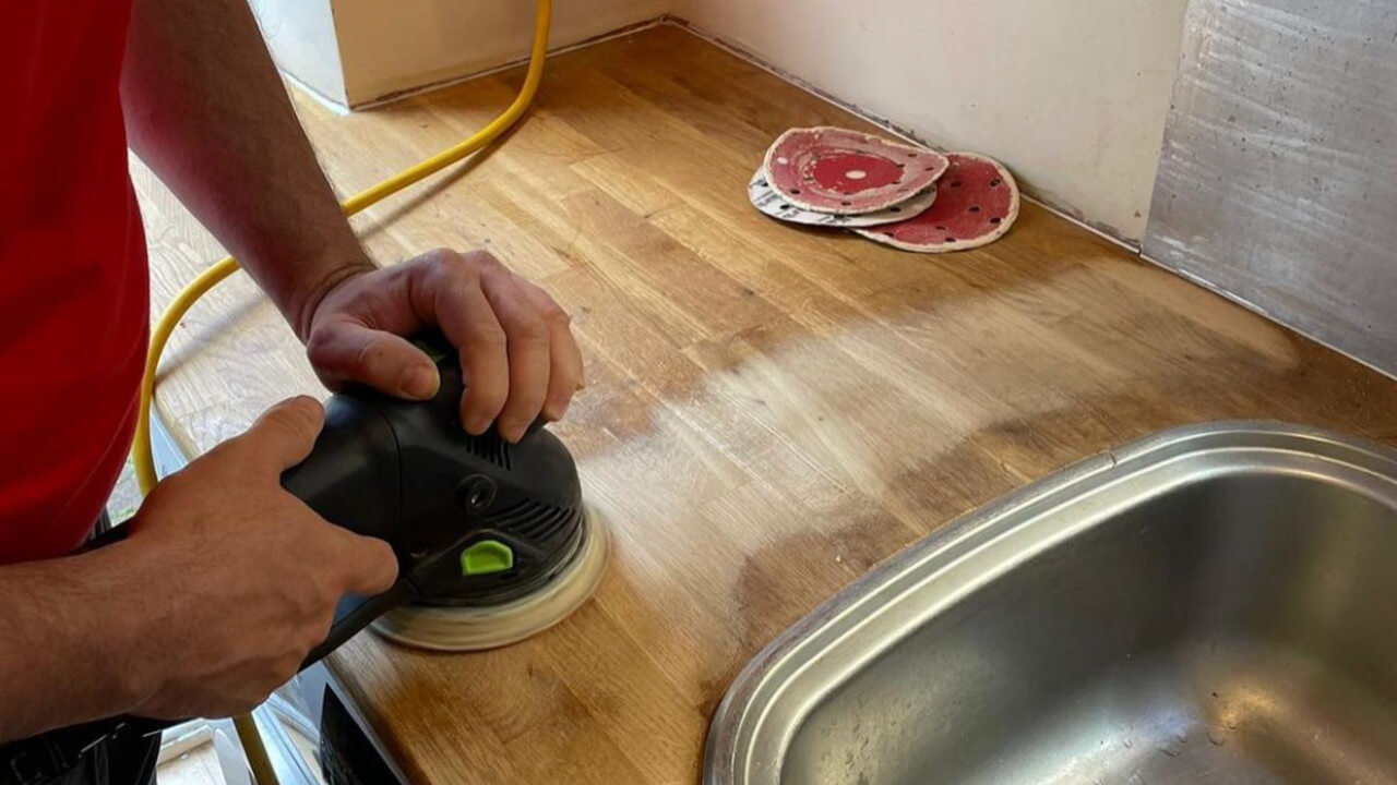 Worktop refinishing in Eltham with a specialist sanding a solid oak kitchen worktop to restore a smooth, hygienic wooden surface.