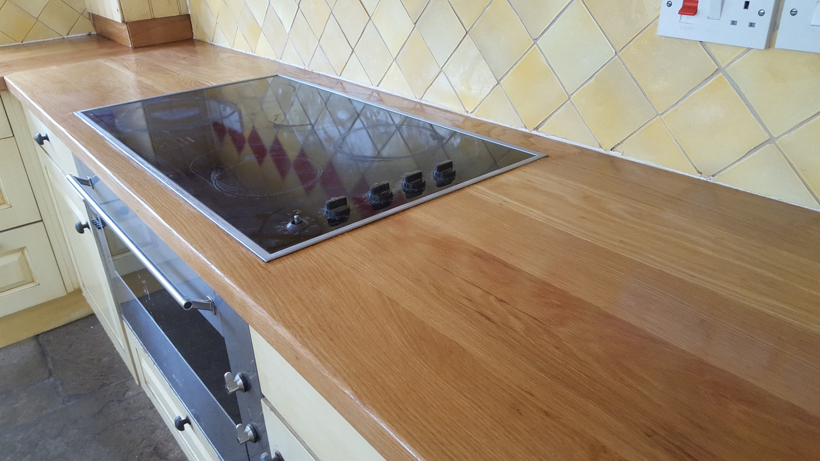 Worktop Refinishing in Eltham with a newly restored solid oak kitchen worktop beside an electric hob and stone tile floor.