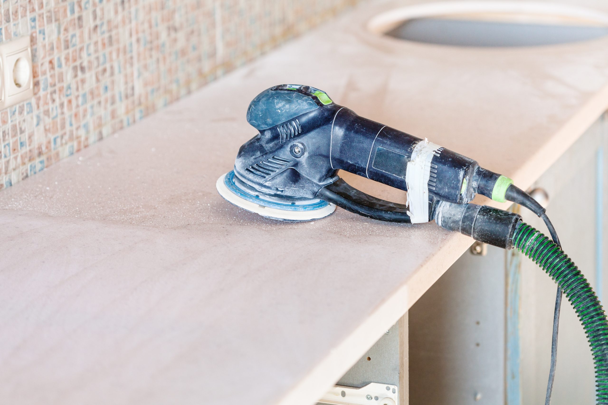 Worktop Refinishing in Eltham with an orbital sander on a solid wood kitchen worktop above a slate tile floor, preparing the surface for a new finish.